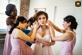 At the Argonaut Hotel in San Francisco, CA, during the getting-ready process, two women assist the bride with her earrings while another adjusts her hair, captured in a moment of care and camaraderie.